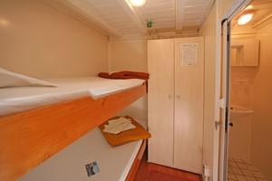 Compact MS Dalmatino cabin with bunk beds, white linens, wooden wardrobe, and view into private bathroom with tiled floor.