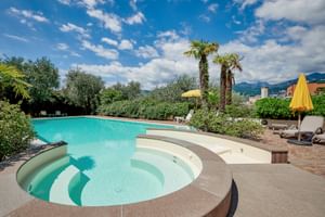 Außenpool mit integriertem Whirlpool im Hotel Catullo in Malcesine, umgeben von Palmen, Sonnenliegen und Bergen im Hintergrund.