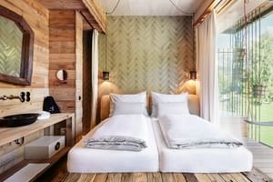 Modern hotel room with twin beds, herringbone wood wall, wooden beams, and glass balcony door at Sepp Alpine Boutique Hotel in Maria Alm.