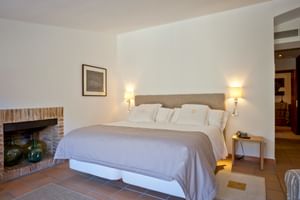 Helles Doppelzimmer mit beigem Polsterbett, weißer Bettwäsche, Terrakottafliesen, Steinkamin und zwei Nachttischlampen im Son Palou Orient.