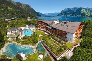 Aerial view of Tirolerhof hotel complex in Zell am See with outdoor pools, gardens, and Lake Zell surrounded by Austrian Alps mountains.