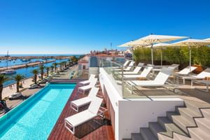 Dachpool-Bereich im Hotel Avenida in Lagos mit weißen Sonnenliegen, Sonnenschirmen und Panoramablick auf Marina und Mittelmeer.