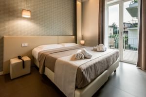 Modernes Hotelzimmer im Palazzo del Garda mit beigem Doppelbett, strukturierter Wand, Nachtwürfeln, Wandlampe und Balkontür.