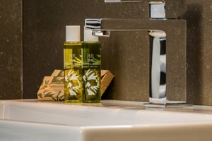 Modernes weißes Waschbecken mit Chromarmatur im Hotel Palazzo del Garda. Zwei grüne Olivenölflaschen und Seife auf Holztablett neben Armatur.