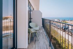 Moderner Hotelbalkon mit weißem Stuhl und kleinem Tisch mit Blick auf Strand und Meer in Porto Covo. Schwarzes Metallgeländer und Holzoptikboden.