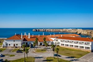 Hotel Pousada Sagres mit weißen Gebäuden und roten Ziegeldächern, Palmen und Küstenklippen mit Blick auf den blauen Atlantik.