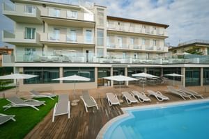 Modernes Hotel Palazzo del Garda Gebäude mit Glasbalkonen und Poolbereich mit weißen Sonnenliegen auf Holzterrasse.