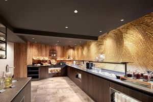 Moderner Frühstücksbereich mit dunklen Holztheken, goldener Wandgestaltung mit Wellenmuster und Brotauslage im Hotel Alte Post Fieberbrunn.