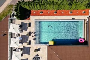 Luftaufnahme des Pools im Hotel Alte Post Fieberbrunn mit türkisfarbenem Wasser, weißen Sonnenschirmen, Liegen und bunten Schwimmreifen.