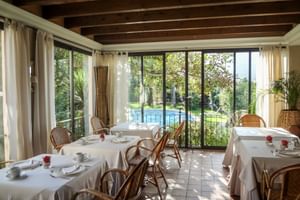 Helles Restaurant im Can Quatre Soller mit weiß gedeckten Tischen, Korbstühlen und großen Fenstern mit Blick auf Pool und Garten.