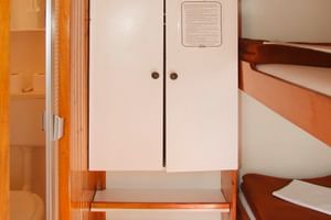 Compact ship cabin with bunk beds, white wardrobe, wooden paneling, and small bathroom. Red carpet covers the floor in this MS Dalmatino cabin.