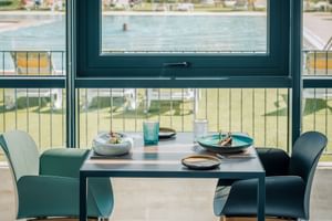 Gedeckter Tisch für zwei mit türkisfarbenen Stühlen mit Blick auf einen Pool im Praia Hotel and Spa in Porto Covo, Sines.