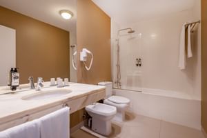 Helles Badezimmer mit beigen Wänden, weißen Armaturen, Badewanne mit Dusche, Bidet, WC und Marmorwaschtisch mit Spiegel im Hotel Pousada Sagres.