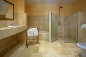 Geräumiges Badezimmer mit beigen Steinfliesen, Glasduschkabine, eingebautem Waschbecken, Handtuchhalter und Bidet im Hotel Son Palou Orient.