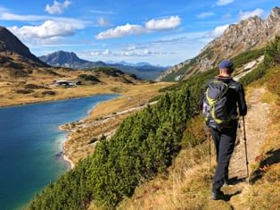 A hiker enjoys the panorama with a view of the alpine hut by the mountain lake