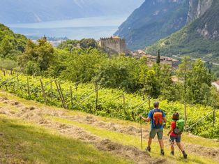 Hiking couple in a field next to a vineyard with a view of the castle and the village of Tenno, Lake Garda in the background