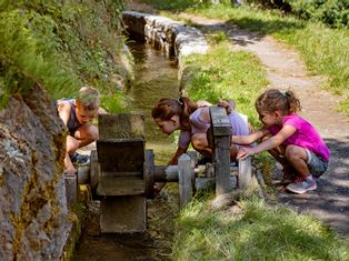 Drei Kinder spielen mit Wasserrad entlang des Wanderweges in Südtirol