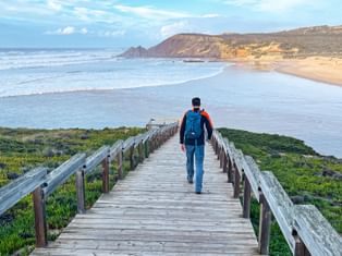 Hikers on a wooden walkway with a view of Praia da Amoreira