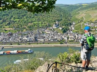 Hiker on the rock of the Loreley with a view of a village and cargo ships on the Rhine