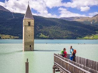Wanderer bewundern den mystischen Reschensee mit seinem versunkenen Kirchturm
