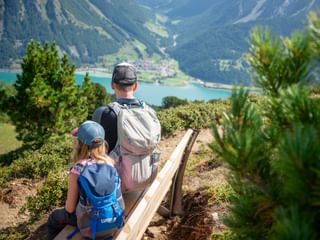Family sitting on a bench and enjoying the panoramic view of Lake Reschen