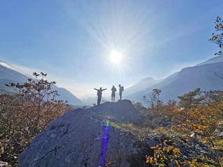 Three hikers in the sunshine on the mountain, one person has his arms outstretched, autumnal nature