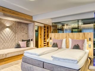 Modernes Doppelzimmer mit zwei Betten, Holzkopfteilen, rosa und grauen Kissen, gepolsterten Wandpaneelen und Holzregalen im Hotel Alte Post Fieberbrunn.