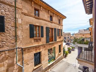 Traditionelles Sandsteingebäude in Pollenca mit grünen Fensterläden und Ziegeldach, mit Blick auf eine ruhige Straße mit mediterraner Architektur.