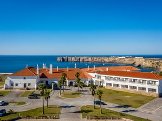 Hotel Pousada Sagres mit weißen Gebäuden und roten Ziegeldächern, Palmen und Küstenklippen mit Blick auf den blauen Atlantik.