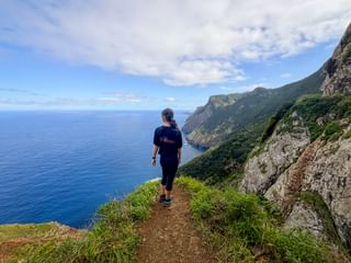 Wanderin auf dem Küstenweg Vereda do Larano auf Madeira mit steilen Klippen, grüner Vegetation und tiefblauem Atlantik.