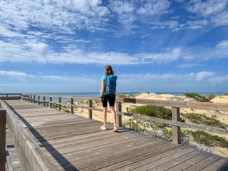 Wanderin wandert am Holzsteg entlang der Praia Verdelago am Meer