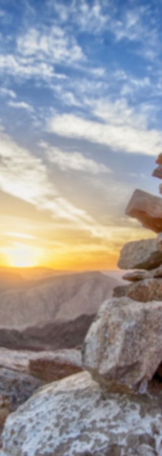Aufgeschichtete Steine vor einer kargen Berglandschaft bei Sonnenuntergang