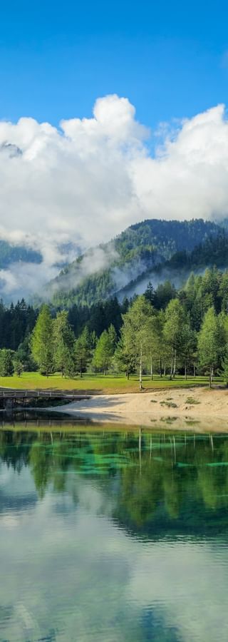 Kristallklarer Jasna See mit smaragdgrünem Wasser, das Berge und Wälder spiegelt. Dichte Nadelwälder umgeben den See in den Julischen Alpen.