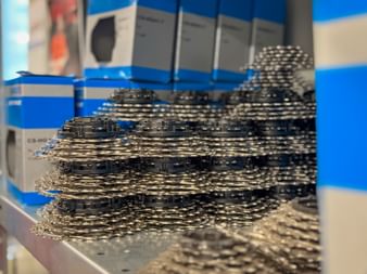 Multiple stacks of black bicycle chains arranged on a white shelf in a bike shop with blue and white product boxes in the background.