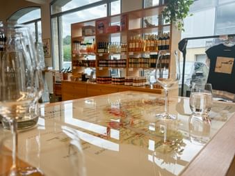 Wine tasting setup at Domäne Wachau in Dürnstein with glasses, carafe, and map on table. Wooden shelves with wine bottles visible in background.