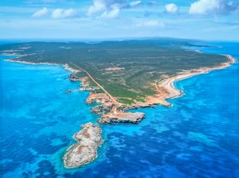 Luftaufnahme der Halbinsel Karpaz auf Zypern mit türkisfarbenem Mittelmeer, grüner Vegetation und felsiger Küste unter blauem Himmel.