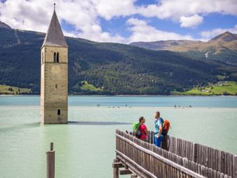 Zwei Wanderer auf einem Steg vor dem Kirchturm von Altgraun im Reschensee