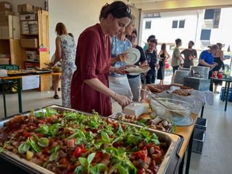 Gäste bedienen sich am Buffet mit Ratatouille und anderen Gerichten beim Eurofun Touristik Sommerfest in einem hellen Büroraum.