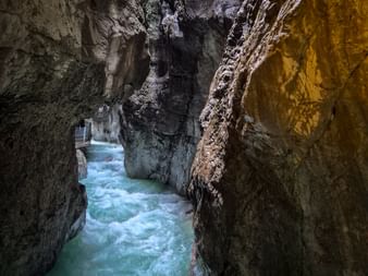 Türkisfarbenes Wasser strömt durch die enge Partnachklamm mit hohen Felswänden und einem Holzsteg auf der linken Seite.