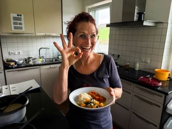 Smiling woman named Petra in modern kitchen holding bowl of colorful vegetables and rice, making OK hand gesture with glasses on.