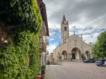 San Giovanni Battista Church in Bossolasco, Piedmont, with stone facade, bell tower, and three arched entrances on a cobblestone square.