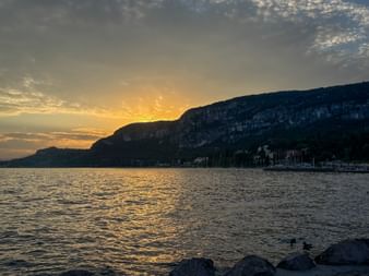 Goldener Sonnenuntergang über dem Gardasee bei Malcesine mit Bergen, die sich gegen den Himmel abzeichnen. Das Wasser reflektiert das warme Licht.