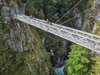 Weiße Metallhängebrücke über die Geisterklamm nahe der Zugspitze. Ein Wanderer überquert die Brücke über Felsklippen und türkisfarbenem Bach.