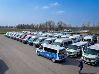 Aerial view of branded vans and minibuses arranged in rows on a parking lot during Eurofun Touristik Training Days 2026, with fields in background.