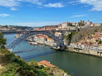 Double-deck metal arch bridge Ponte Luís I spanning the Douro River in Porto with historic old town buildings on hillside and boats in the water.