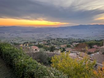Sonnenuntergang über Volterra mit Terrakottadächern und toskanischen Hügeln. Goldenes Licht beleuchtet das Tal unterhalb der Hügelstadt.