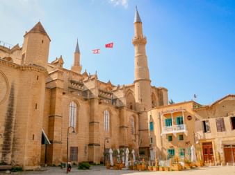 Gotische Kathedrale in Nikosia mit zwei hohen Minaretten und Steinfassade. Traditionelle mediterrane Gebäude mit blauen Fensterläden unter klarem Himmel.