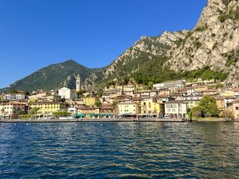 Bunte Gebäude von Limone sul Garda am blauen Wasser des Gardasees mit dramatischen Bergklippen hinter der Stadt.