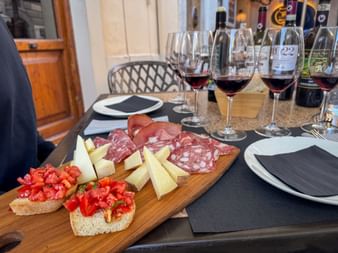 Weinprobe in Castellina mit Rotweingläsern, Holzbrett mit Käse, Salami und Bruschetta mit Tomaten auf einem Tisch.
