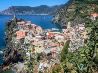 Aerial view of Vernazza, a colorful village in Cinque Terre, nestled on rocky cliffs with a small harbor, surrounded by blue sea and mountains.